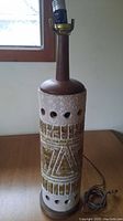 Full lamp showing glazed ceramic body with carved geometric patterns, teak wood top and base, and electrical socket.