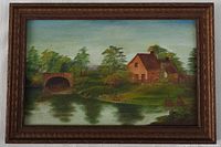 Framed oil painting on board showing a river with a stone bridge to the left and two beige houses with brown roofs in the background, surrounded by trees and greenery.