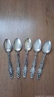 Photo of five sterling silver spoons arranged side by side, showing the full length of each spoon with visible tarnish.