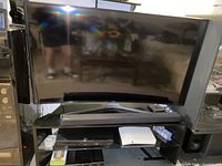 Photo of Samsung 55 inch curved UHD TV set up on a black TV stand with a soundbar in front. Remote control is also on the shelf.