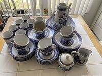 Blue and white Willow Ware porcelain tableware pieces arranged including cups, saucers, plates, creamer, sugar bowl, and teapot