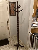 Full view of the tall, dark wood jacket hanger with twisted pole and curved tripod base in entryway