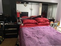 Photo of black lacquered bedroom suite showing bed with red pillows and blanket, mirrored headboard with built in lighting, and black lacquered two drawer units on each side captured in light reflecting room.