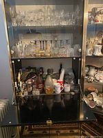 Front open view of black-lacquered glass cocktail cabinet showing glassware and bar items inside