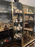 Front view of the tall glass display cabinet showing multiple shelves with glassware and porcelain items inside.