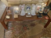 Wooden center table with multiple decorative items on top including glass angel figurines, photo frames, a clock, paperweights, and a lantern