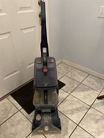 Full front view of Hoover Power Scrub Carpet Cleaner standing upright against a door on tiled floor.