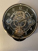 Front view of the black clock showing the gear design, clock hands, temperature gauge, and hygrometer.