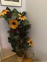 Full view of the artificial sunflower plant showing five yellow flowers and green leaves in woven pot next to wall and floor.