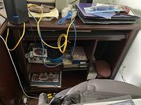 Wooden computer desk with laptop and office items on top, various cables and objects in storage shelves below.