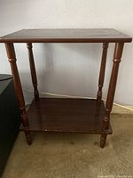 Front view of one wooden side table showing turned legs and lower shelf