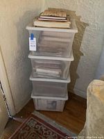 Stack of four clear plastic bins filled with books in a corner by a wall with partially peeled paint