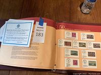 Open binder album on wooden table showing pages with multiple U.S. commemorative stamps mounted and postmarked