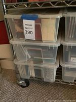 Three plastic bins stacked on metal shelving containing numerous CDs in jewel cases and other formats.