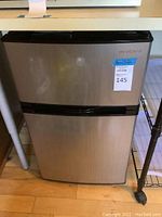 Closed mini refrigerator showing brushed stainless steel front and Insignia branding.
