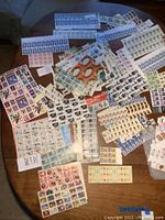 Photo displaying a wide assortment of sheets and strips of collectible stamps laid out on a table, with diverse designs including portraits and holiday themes.