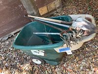 Photo showing green plastic wheelbarrow containing garden tools including shovel and aerator