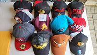 13 hats arranged in three rows with visible logos including Chicago Blackhawks, Canada, Arizona State Sun Devils, and others