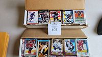 Photo showing overview of assorted hockey and baseball trading cards in boxes and stack, revealing cards with different players and team uniforms