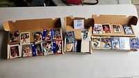Three boxes containing assorted sports trading cards including basketball, hockey, and baseball in plastic sleeves and loose.