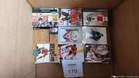 Top-down view of multiple small stacks of hockey cards in a cardboard box showing player images from Calgary Flames, New Jersey Devils and others.