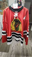 Front view of red Chicago Blackhawks hockey jersey with lace-up collar and large team logo on front.