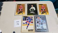 Top-down photo of 5 hockey cards on a white table: two identical Stan Mikita Beehive cards with yellow borders, a Wayne Gretzky card in New York Rangers uniform, a Bobby Hull Upper Deck Masterpieces card, and a close-up of Belfour card with black background and gold foil.