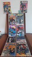 Lot of 10 vintage Batman and Detective Comics comics arranged on a small table and against a wall, showing various cover art including Batman in action poses and group scenes.