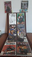 10 Batman comic books arranged in two columns laid out on a dark surface, visible covers show characters like Bane and Batman with a mix of color and black and white covers. Comics in protective sleeves.