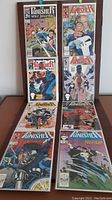 Eight bagged and boarded The Punisher War Journal comics displayed upright inside a wooden rack. Covers show various action scenes and characters including The Punisher.