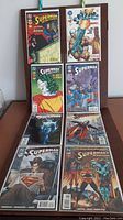 Eight Superman-themed comic books arranged in two columns on a board, showing front covers with colorful modern and classic superhero artwork.