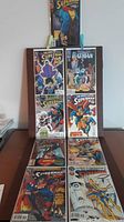 Photo showing nine Superman comics arranged on a table with visible covers featuring superheroes in various action scenes.