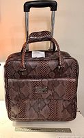 Full front view of brown snake print rolling laptop bag showing handles, wheels, and front snap pocket.