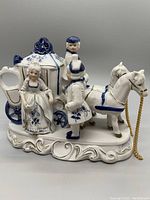 Front and side view of blue and white porcelain horse-drawn carriage figurine with figures.