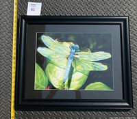 Front view of framed artwork showing dragonfly on leaves with ruler for size reference.