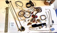 Overview of all costume jewellery items including necklaces, bracelets, and brooches laid out on white surface with ruler for size reference.
