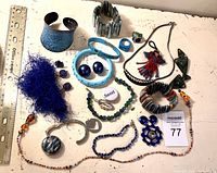 Top-down view of the costume jewelry items spread flat on a white surface with a ruler for scale. Various bracelets, necklaces, rings and pendants visible.
