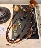 Overview of all costume jewelry pieces laid out on black board including necklaces, brooches, bracelet, and earrings with ruler for scale