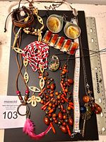 Photo showing multiple costume jewellery pieces including necklaces, bracelet and earrings arranged on a flat surface next to a ruler for scale.