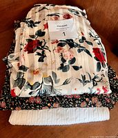 Folded stack of three clothing items showing floral print, dark floral fabric, and white quilted fabric