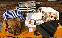 Six bags displayed on a bench outdoors with brick background.