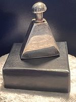 Miniature bottle with a tapered square base and rounded stopper on black box.