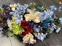 Mixed color artificial flower bunch showing various blue, cream, red, purple, and green flowers lying on a floor.