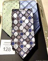 Three neckties laid flat on a black display with a ruler and lot tag visible, showing the tie patterns.
