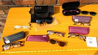 Full lot of assorted reading glasses and sunglasses with multiple cases placed on a wooden table