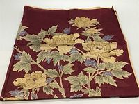Front view of the silk scarf showing a deep burgundy background with large yellow flowers and green leaves with gold outlining.