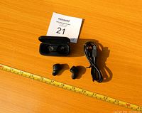 Skullcandy wireless earbuds shown outside charging case, case and charging cable on wooden surface with measuring tape for scale.