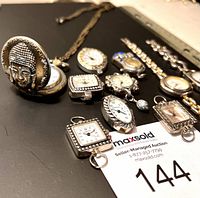 Photo showing multiple assorted vintage-style timepieces including pendant watches with decorative covers, wristwatches with rhinestone details, and linked bracelet watches laid out on a surface with a ruler for scale.