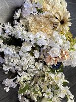 Close-up photo of white and cream artificial flowers including daisies, hydrangeas, lilies, and roses.