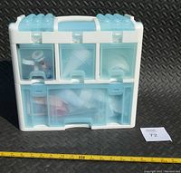 Closed plastic organizer case with multiple compartments, blue and white translucent lid, placed on black rubber background with measuring tape visible.